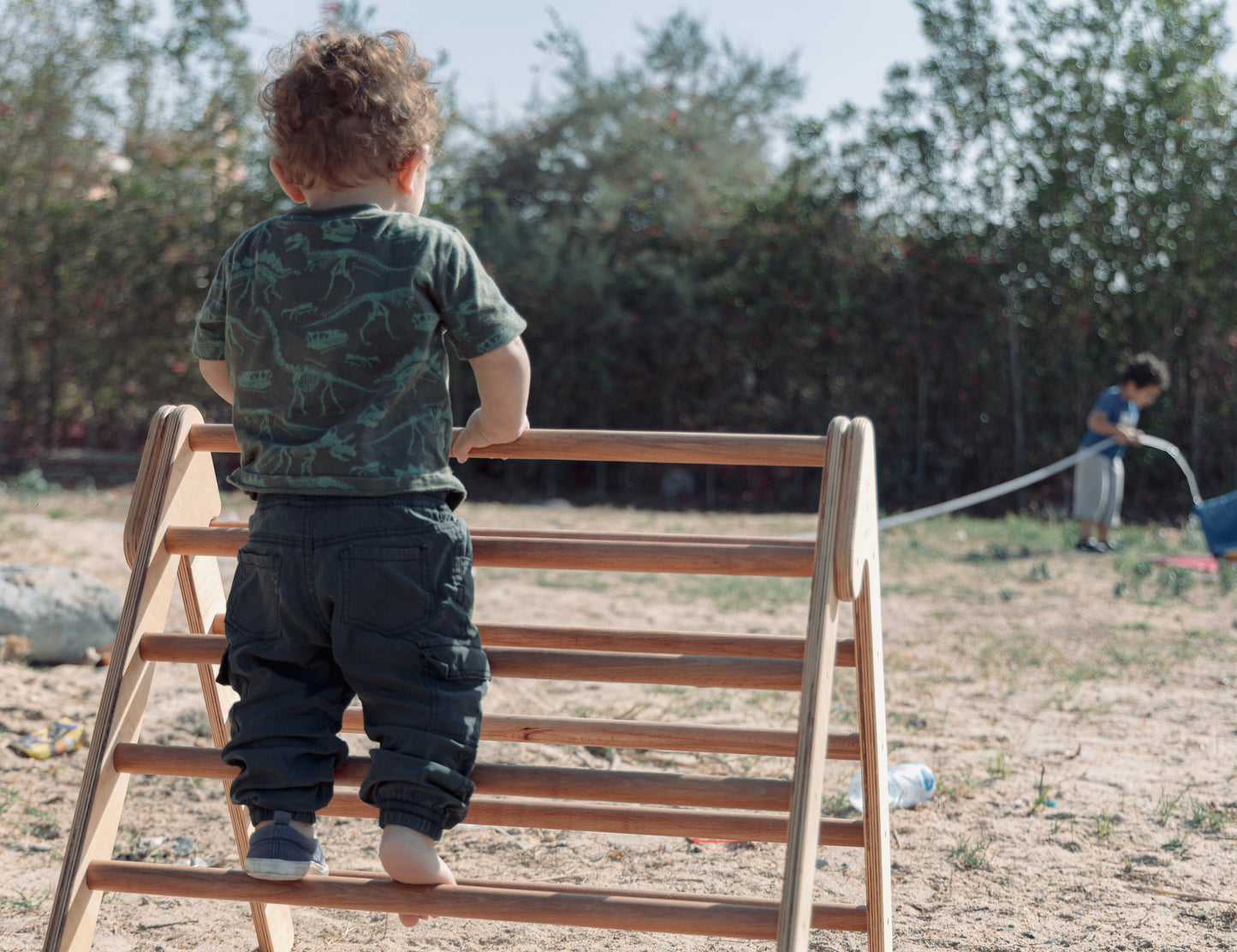 2 Children playing in the garden. One boy is climbing on the Pikler-Triangle. The other boy is watering the grass.